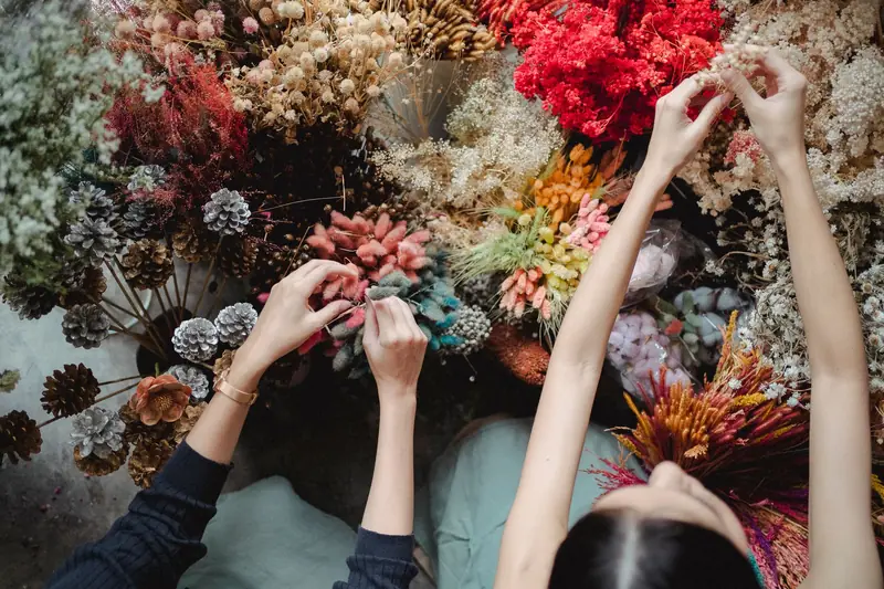 Hands arranging fresh and dried flowers on a workbench